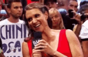 a woman in a red dress is holding a microphone and smiling in front of a crowd .