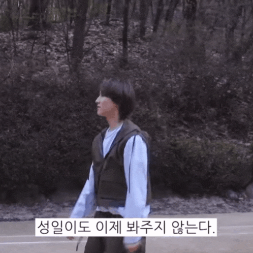 a person in a vest is standing in front of trees and a sign that says ' 생일 '