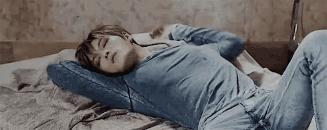 a young man in a blue shirt and jeans is laying on a bed .