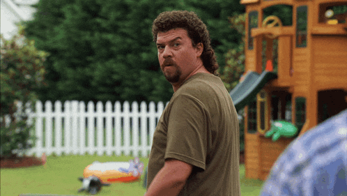 a man with a mullet and a beard is standing in front of a playground