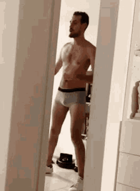 a shirtless man in boxer shorts is standing in a hallway in front of a mirror .