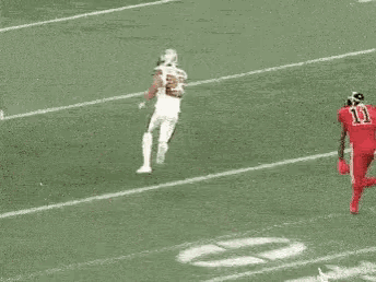a group of football players are running on a field . one of the players has the number 11 on his jersey .