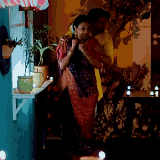 a man in a yellow shirt is hugging a woman in a red saree