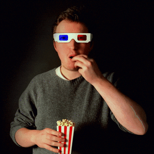 a man wearing 3d glasses and eating popcorn