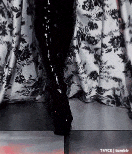 a woman wearing black boots is standing in front of a floral curtain