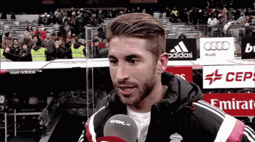 a soccer player is talking into a microphone in front of a sign that says adidas