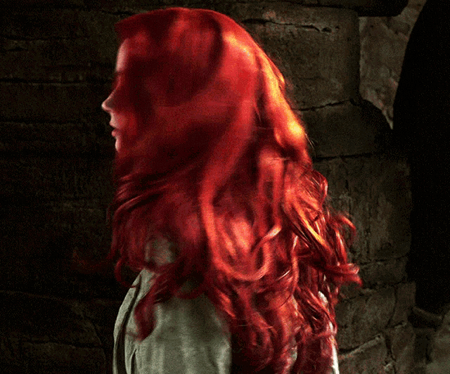 a woman with red hair is standing in front of a brick wall