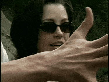 a woman wearing sunglasses holds out her hand towards a man