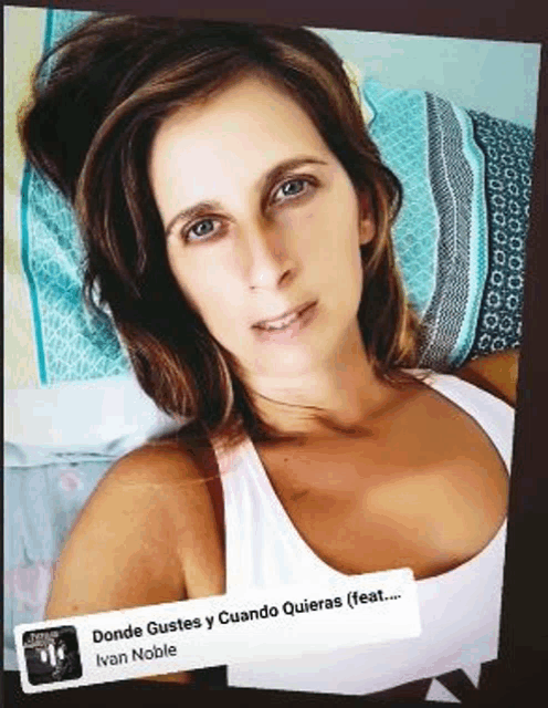 a woman in a white tank top is laying on a bed with a blue and white pillow .