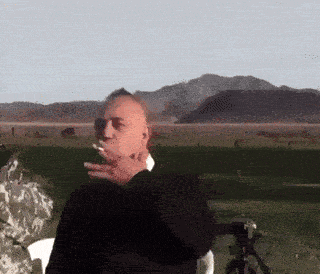 a man smoking a cigarette in front of a mountain range