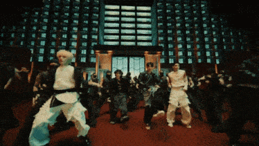 a group of people are dancing in front of a building with many windows