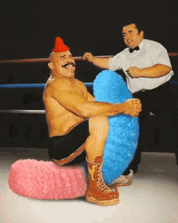 a wrestler with a red hat is sitting on a pink and blue pillow