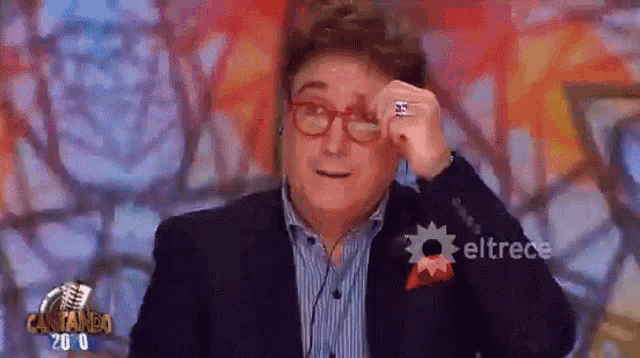 a man wearing glasses and a ring is on a television screen with eltrece written in the corner