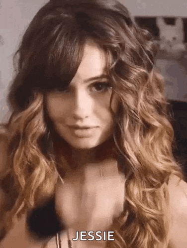 a woman with long curly hair and bangs is wearing a choker necklace and looking at the camera .