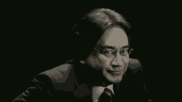 a man wearing glasses and a suit smiles in the dark