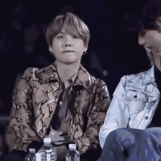 a man in a snakeskin jacket sits next to another man