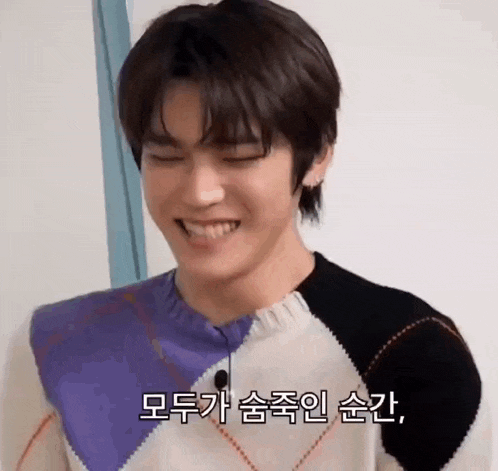 a young man is wearing a sweater and smiling with korean writing on it .