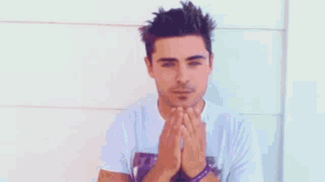 a man is sitting in front of a white wall holding his hands together .