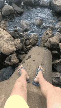 a person wearing flip flops is standing on a rock near a river