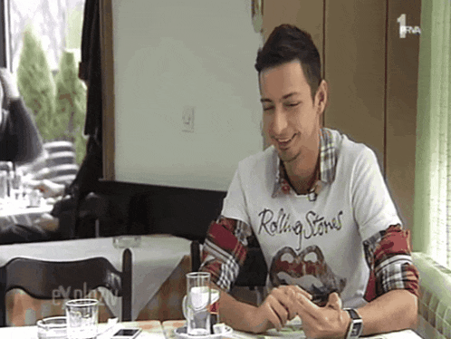 a man wearing a rolling stones t-shirt sits at a table