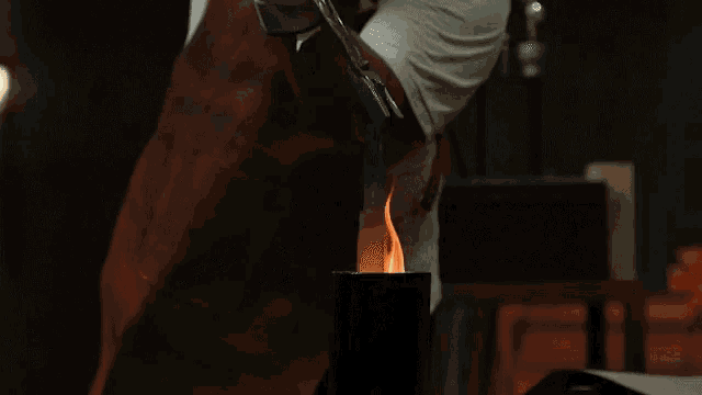 a man in an apron is holding tongs over a pot of flames
