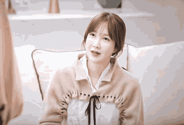 a woman wearing a sweater and a white shirt sits on a white couch