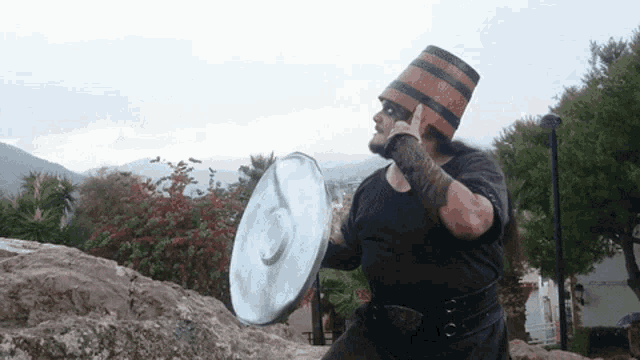 a man wearing a barrel hat holds a shield