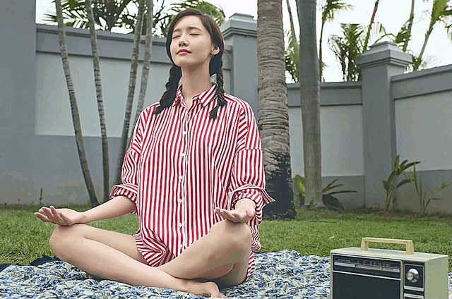 a woman in a red and white striped shirt sits in a lotus position