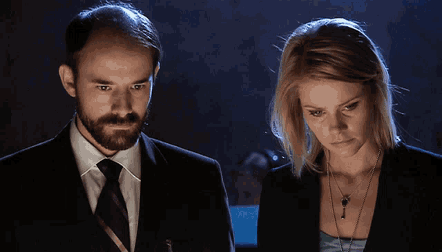 a man in a suit and tie stands next to a woman with blonde hair