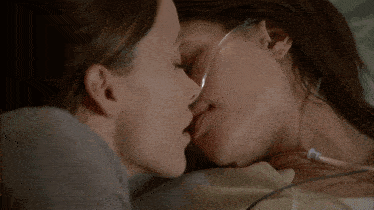 two women kissing in a hospital bed with an oxygen tube in their ear