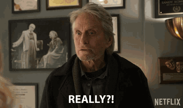 a man with a beard says really in front of a wall of framed pictures