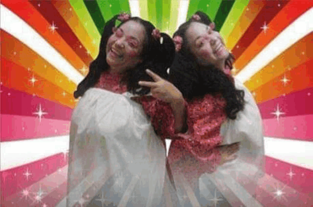 a couple of women are standing next to each other in front of a rainbow background .