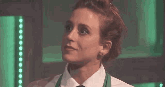 a woman wearing a green apron and a white shirt is looking at the camera .