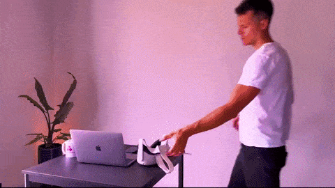 a man in a white shirt is standing in front of a desk with an apple laptop on it