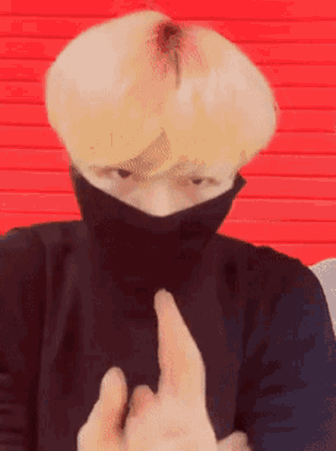 a man with blonde hair wearing a black turtleneck and a black mask on his face giving the middle finger