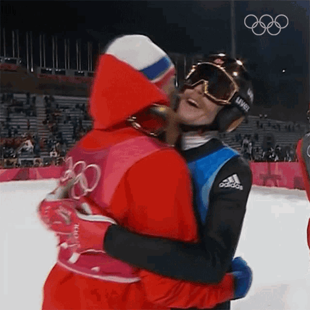two athletes hugging each other in front of a sign that says olympics