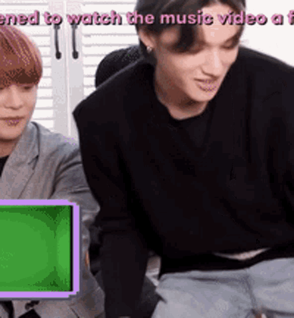 a man and a woman are sitting in front of a green screen that says " ened to watch the music video "