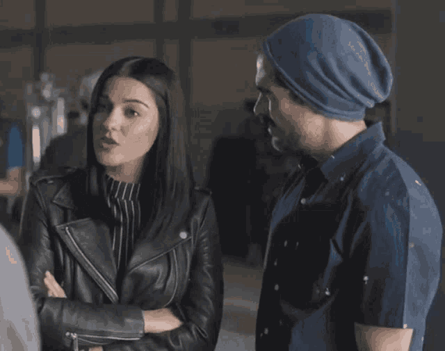 a man wearing a blue beanie talks to a woman