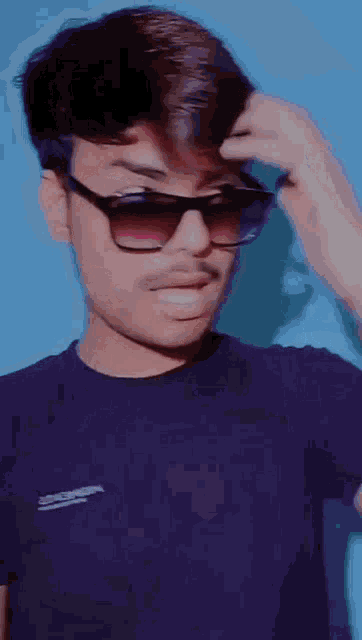 a boy wearing sunglasses and a purple shirt has his hand on his hair