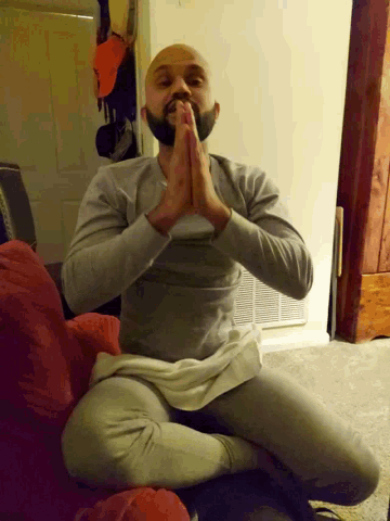 a man with a beard is sitting on the floor with his legs crossed and his hands folded