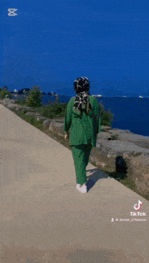 a woman in a green outfit is walking down a sidewalk with a red sign that says yaş