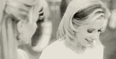 a woman is smiling in a black and white photo while standing next to another woman .