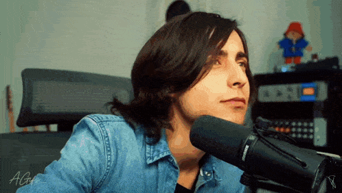 a young man in a denim shirt is sitting in front of a microphone with the letters ag on his shirt