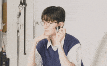 a young man wearing glasses and a blue vest holds a magnifying glass to his face