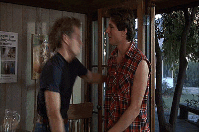 two men are standing next to each other in a room in front of a window .