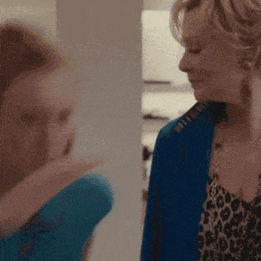 a woman wearing a blue jacket and a leopard print top is talking to another woman