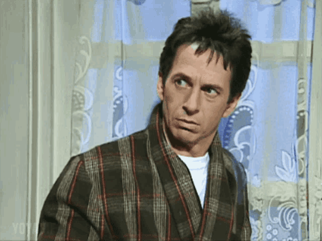 a man wearing a plaid robe looks out a window