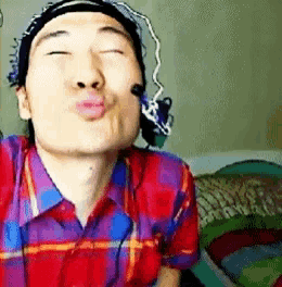 a man in a plaid shirt is blowing a kiss with his eyes closed