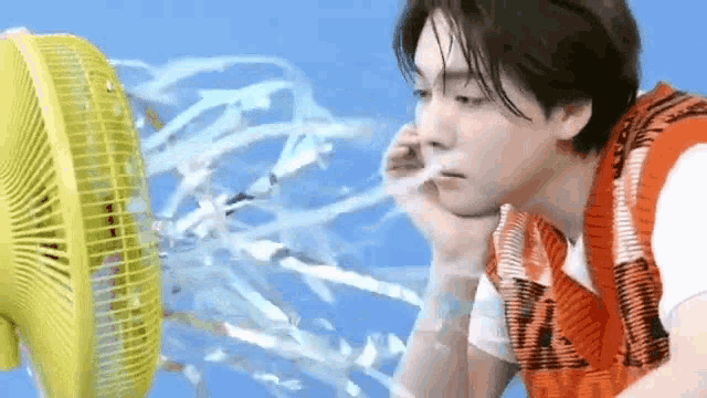 a man is sitting in front of a yellow fan with water coming out of it