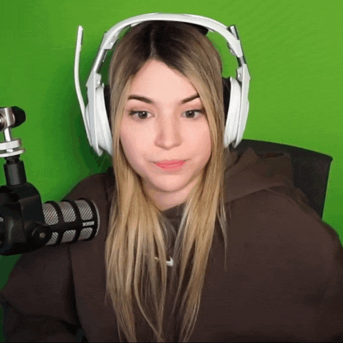 a woman wearing headphones and a brown hoodie stands in front of a green screen